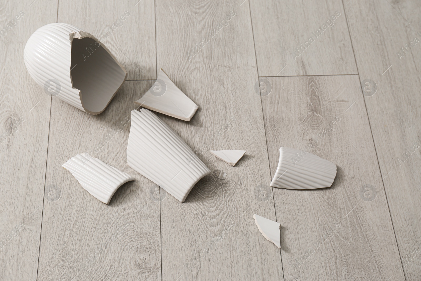 Broken white ceramic vase on wooden floor Photo of Broken white ceramic vase on wooden floor