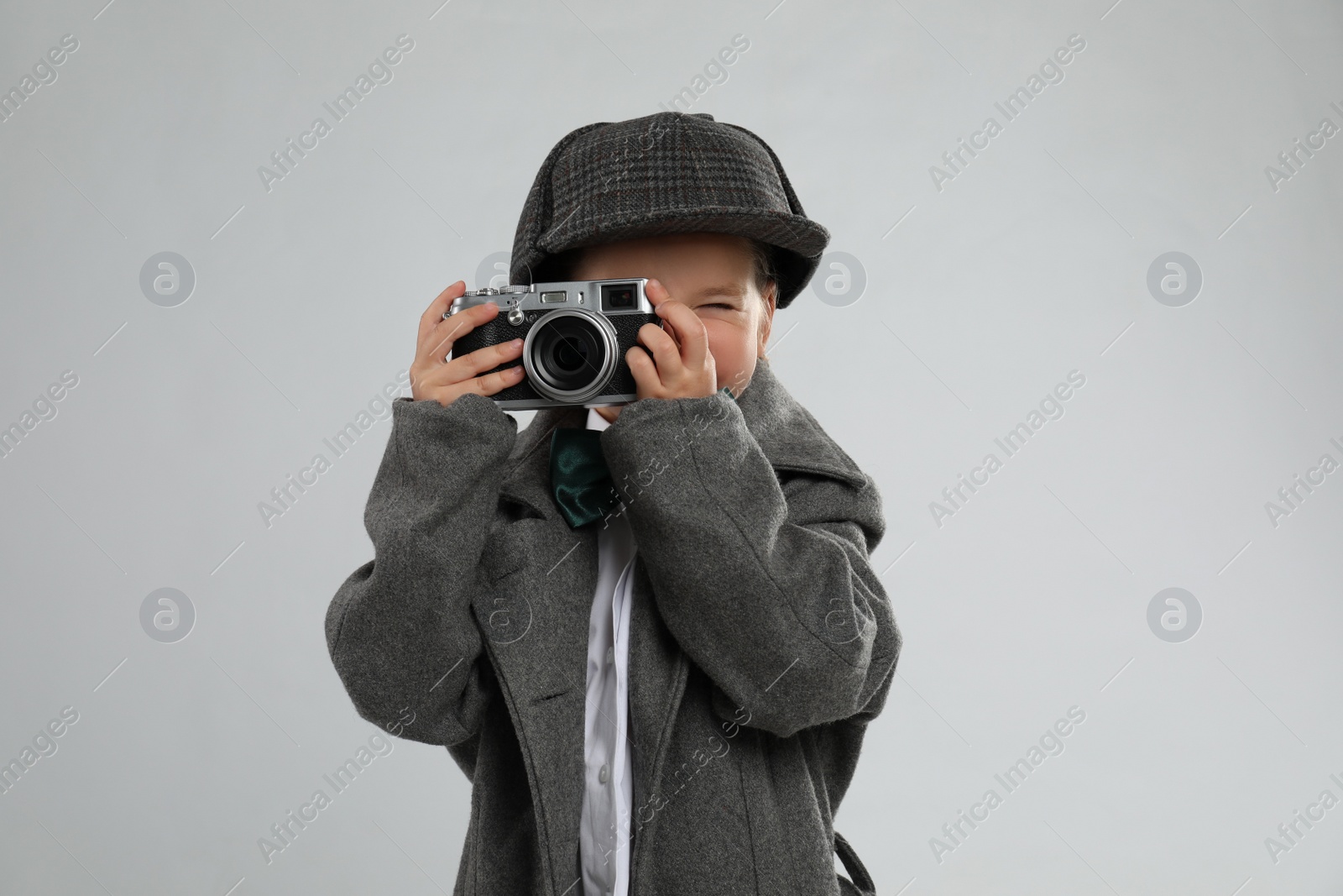 Cute little detective taking photo with vintage camera on grey background Photo of Cute little detective taking photo with vintage camera on grey background