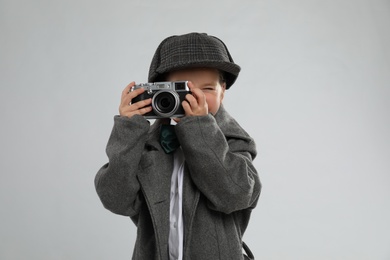 Photo of Cute little detective taking photo with vintage camera on grey background