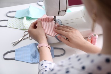 Woman making cloth mask with sewing machine at white table, closeup Photo of Woman making cloth mask with sewing machine at white table, closeup