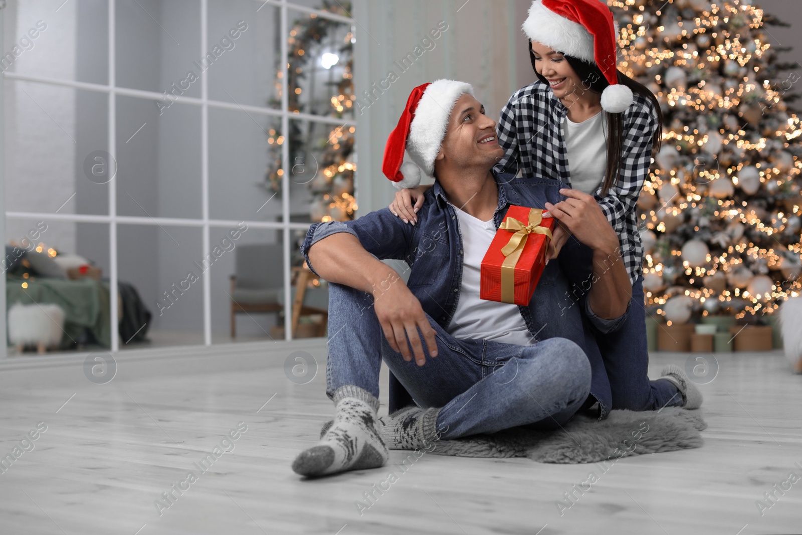 Happy young couple in Santa hats with Christmas gift at home Photo of Happy young couple in Santa hats with Christmas gift at home