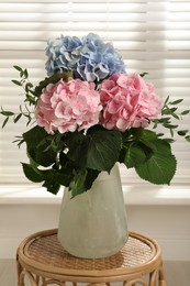 Beautiful hortensia flowers in vase on wicker stand indoors Photo of Beautiful hortensia flowers in vase on wicker stand indoors