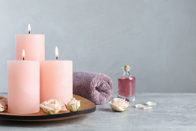 Burning candles, roses, essential oil and towel on grey table Photo of Burning candles, roses, essential oil and towel on grey table