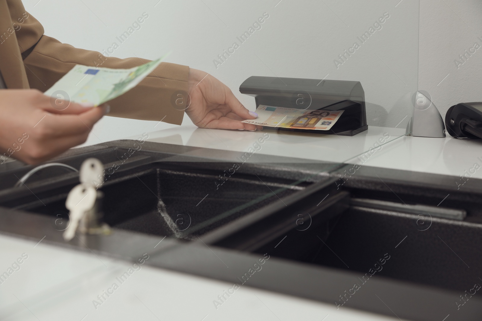 Cashier checking money with currency detector at exchange department, closeup Photo of Cashier checking money with currency detector at exchange department, closeup