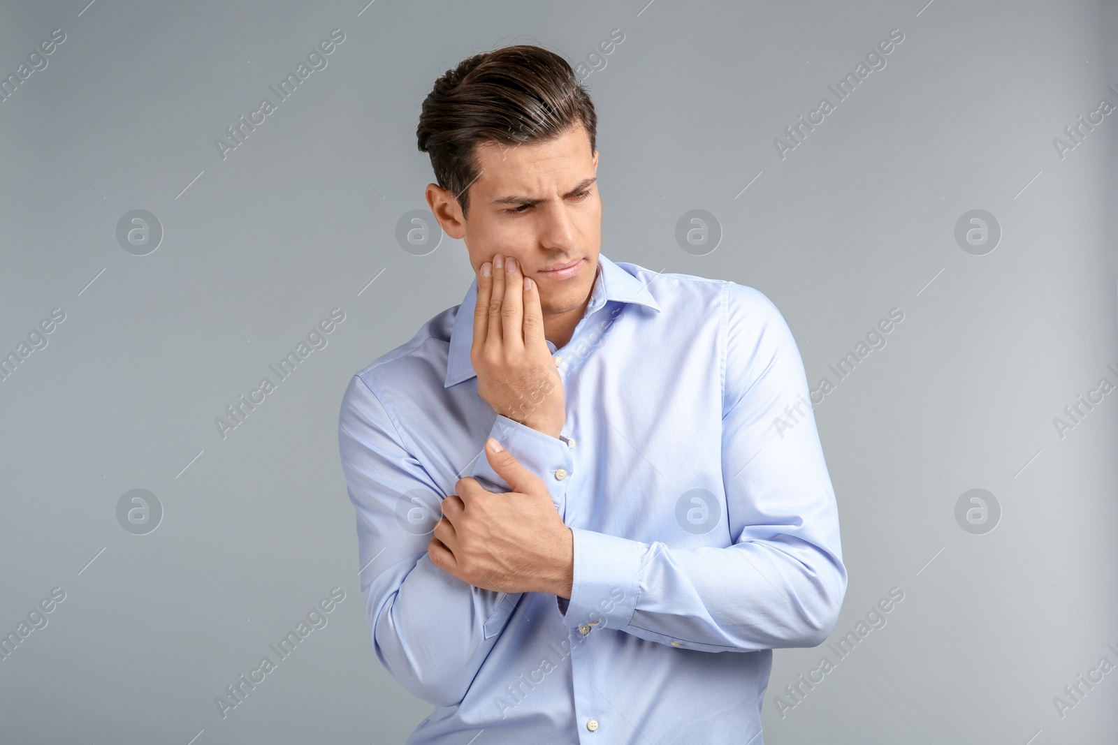Young man suffering from toothache on grey background Photo of Young man suffering from toothache on grey background