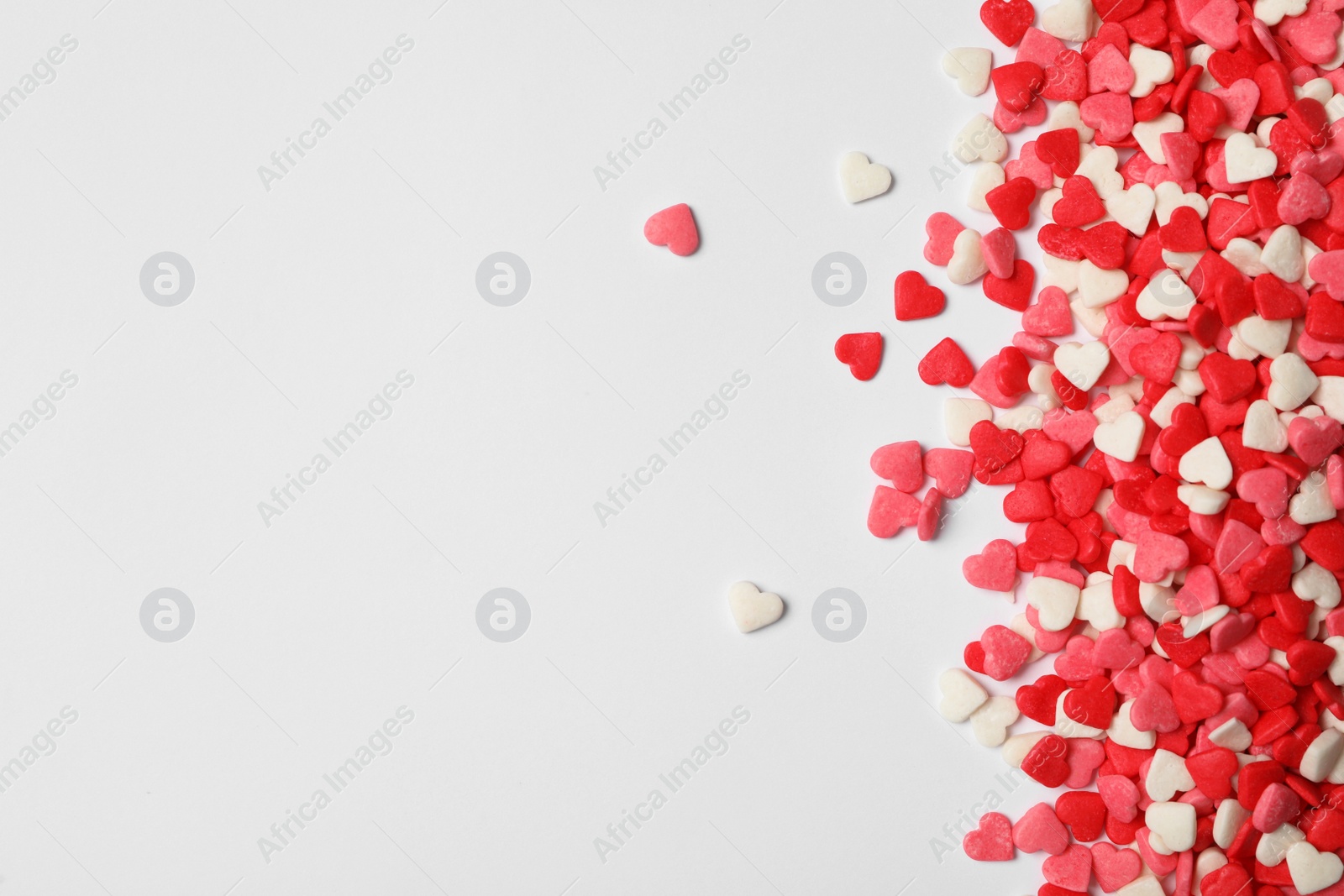 Bright heart shaped sprinkles on white background, flat lay. Space for text Photo of Bright heart shaped sprinkles on white background, flat lay. Space for text