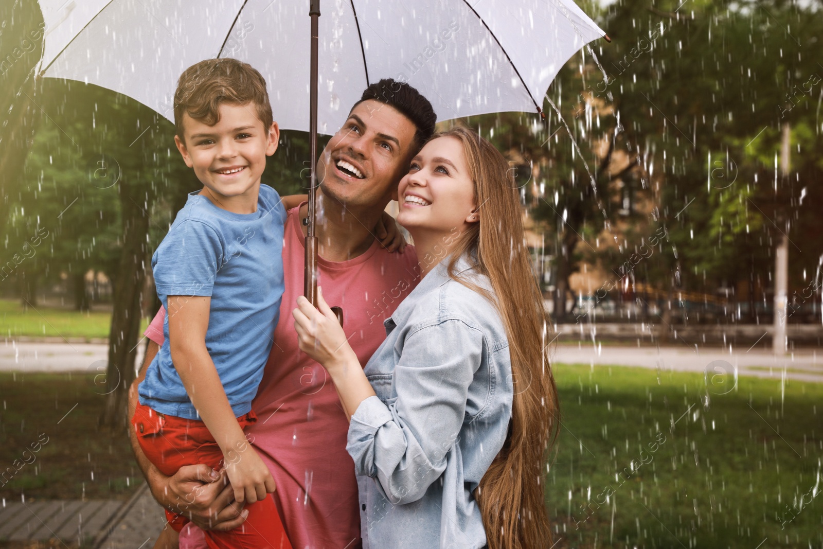 Happy family with umbrella walking under rain in park Photo of Happy family with umbrella walking under rain in park