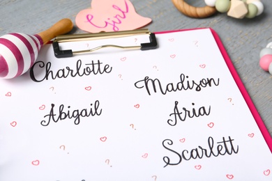 Clipboard with different baby names and toys on grey table, closeup Photo of Clipboard with different baby names and toys on grey table, closeup