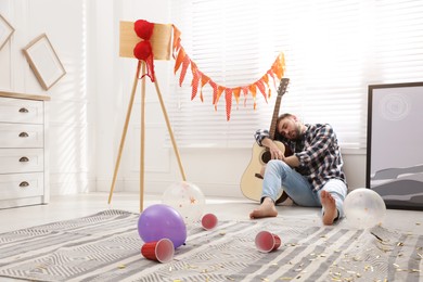 Young man with guitar sleeping near window in messy room after party Photo of Young man with guitar sleeping near window in messy room after party