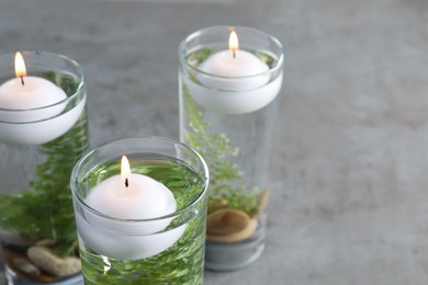 Candles, stones and fern leaves in glass holders with liquid on grey table, closeup Photo of Candles, stones and fern leaves in glass holders with liquid on grey table, closeup