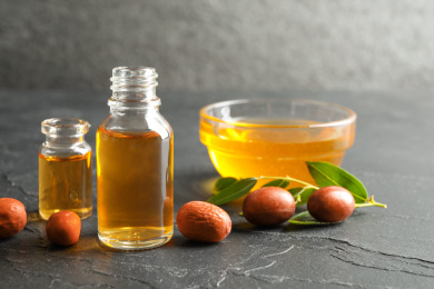 Jojoba oil and seeds on dark grey table Photo of Jojoba oil and seeds on dark grey table