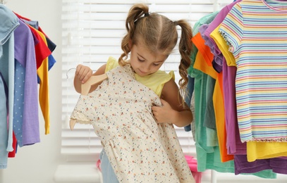 Little girl choosing clothes on racks indoors Photo of Little girl choosing clothes on racks indoors
