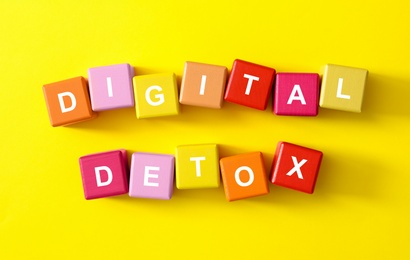 Colorful cubes with phrase DIGITAL DETOX on yellow background, flat lay Photo of Colorful cubes with phrase DIGITAL DETOX on yellow background, flat lay