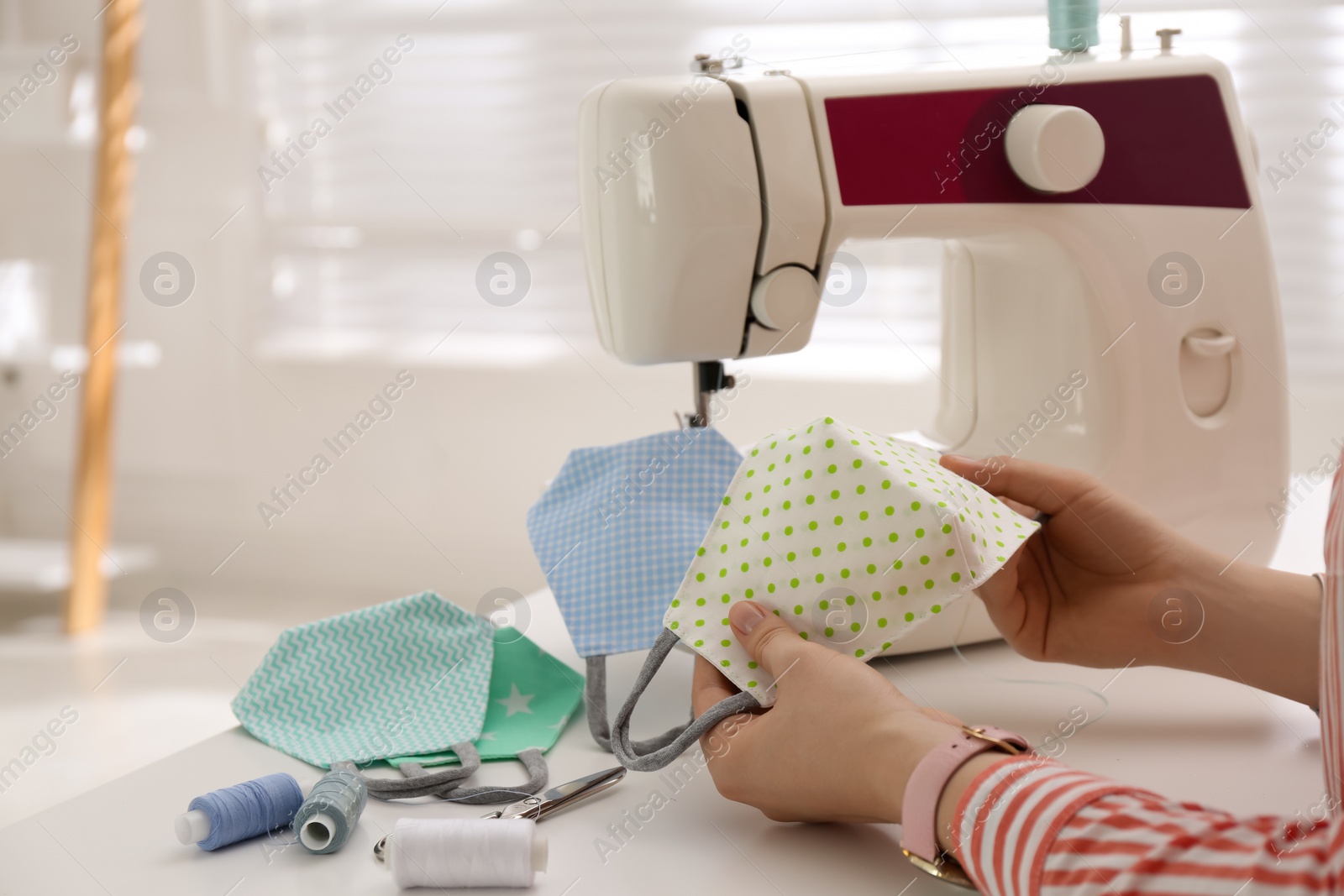 Woman making cloth mask with sewing machine at white table, closeup Photo of Woman making cloth mask with sewing machine at white table, closeup