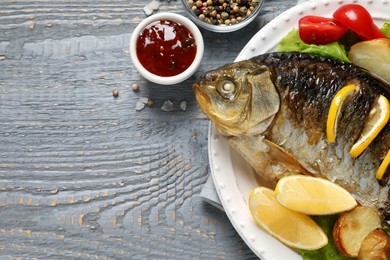 Tasty homemade roasted crucian carp served on grey wooden table, flat lay and space for text. River fish Photo of Tasty homemade roasted crucian carp served on grey wooden table, flat lay and space for text. River fish