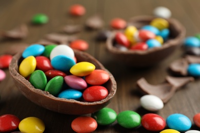 Broken chocolate egg and colorful candies on wooden table, closeup Photo of Broken chocolate egg and colorful candies on wooden table, closeup