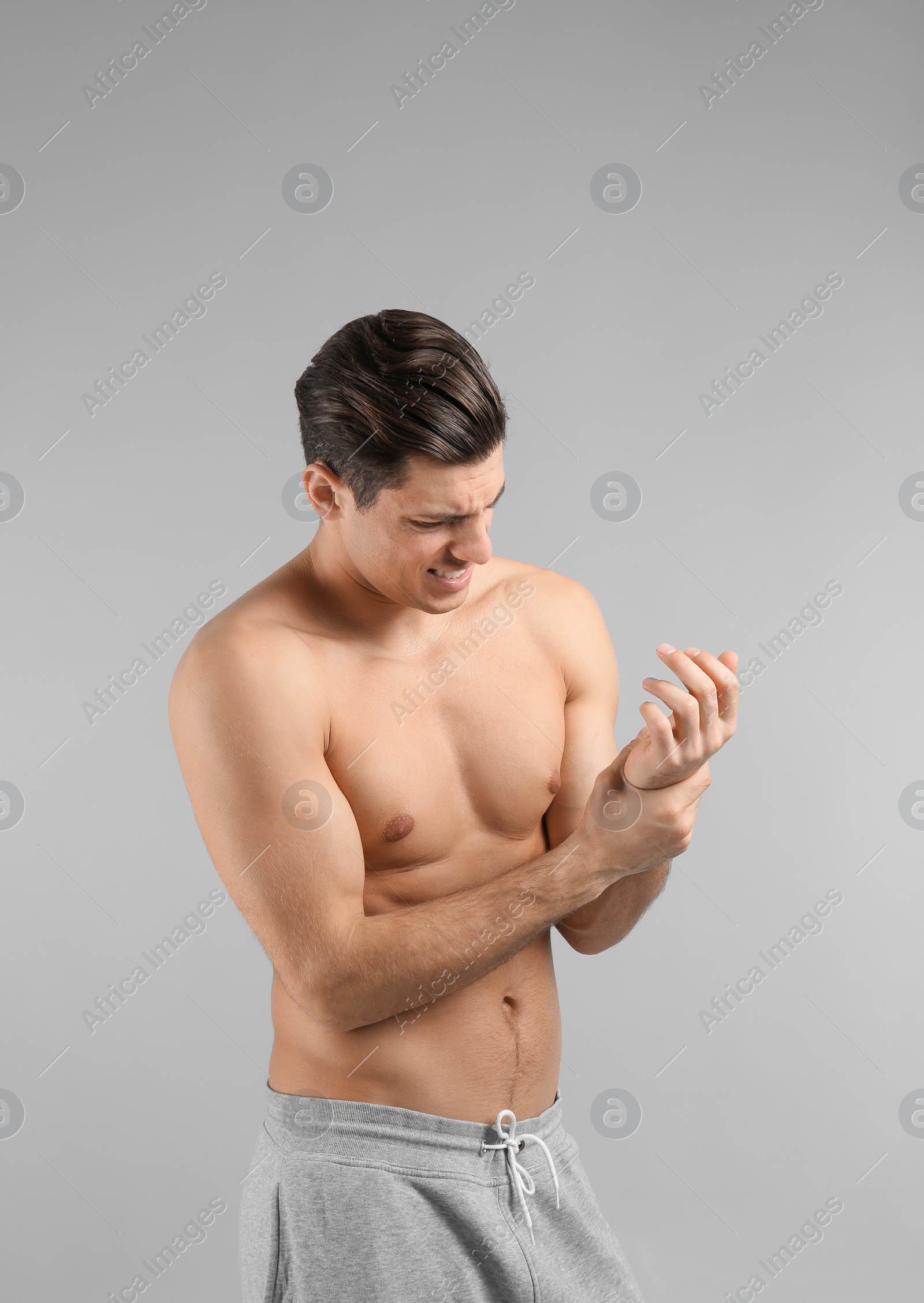 Young man suffering from pain in wrist on grey background Photo of Young man suffering from pain in wrist on grey background