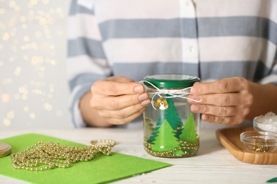 Photo of Woman making snow globe at white table, closeup