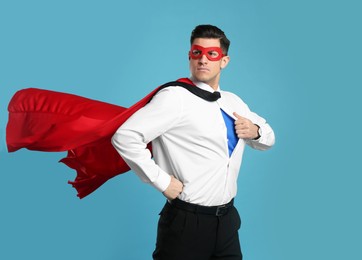 Businessman in superhero cape and mask taking shirt off on light blue background Photo of Businessman in superhero cape and mask taking shirt off on light blue background