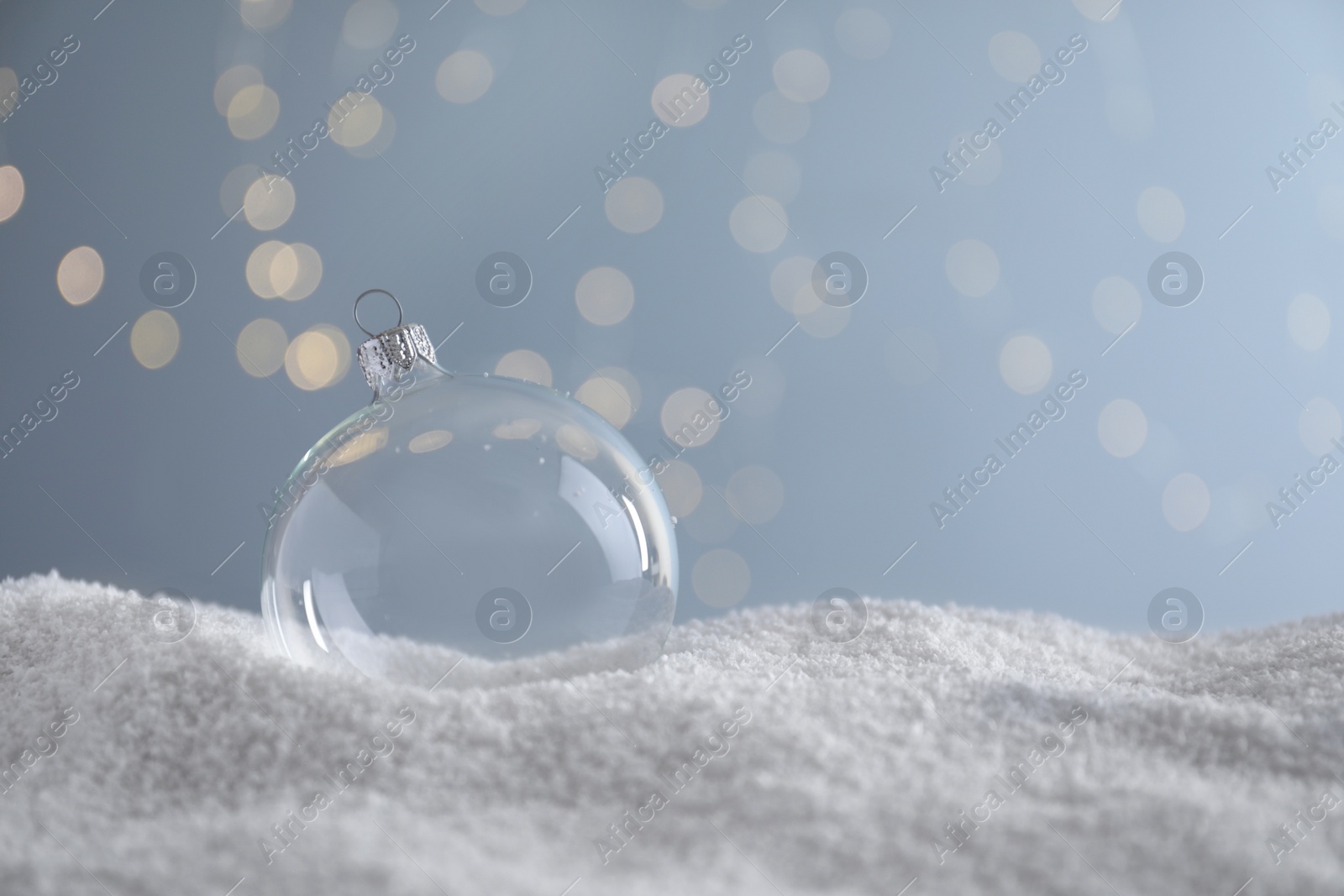Transparent Christmas ball on snow against blurred fairy lights, space for text Photo of Transparent Christmas ball on snow against blurred fairy lights, space for text
