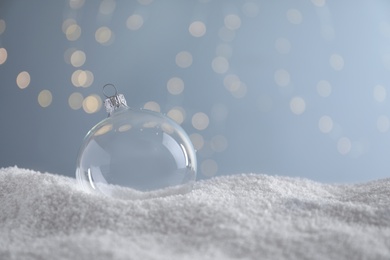 Transparent Christmas ball on snow against blurred fairy lights, space for text Photo of Transparent Christmas ball on snow against blurred fairy lights, space for text