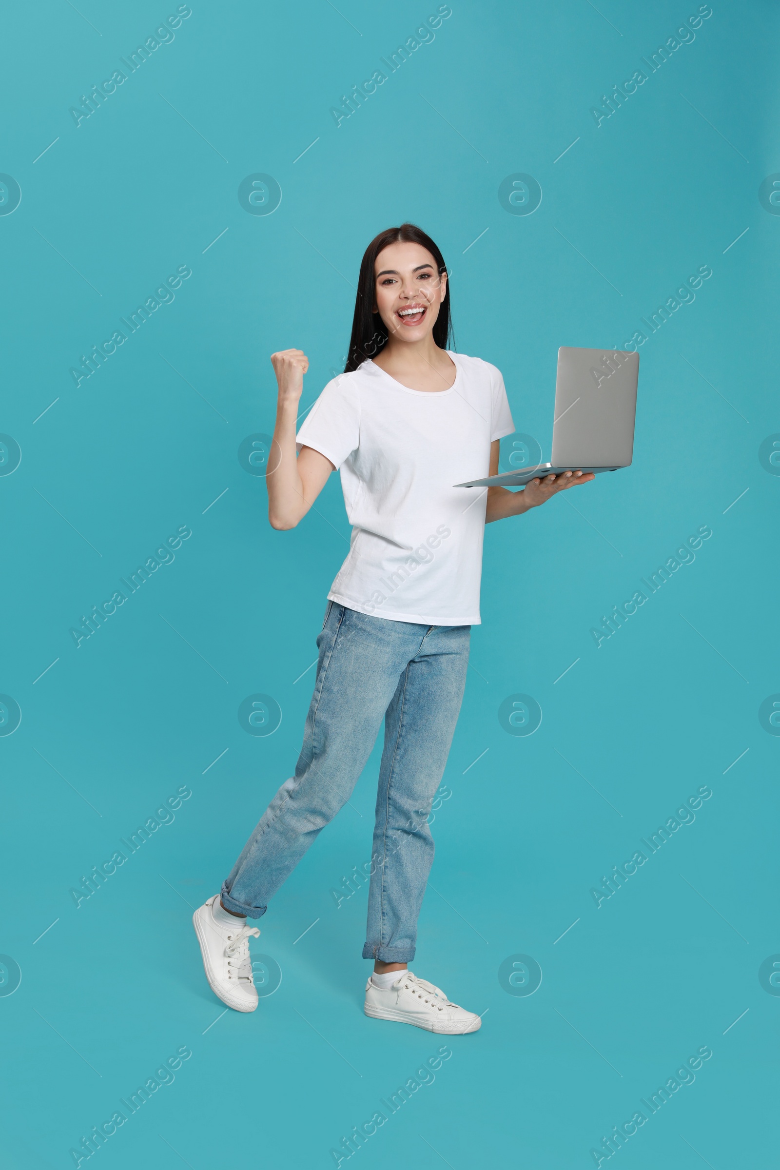 Emotional young woman with modern laptop on light blue background Photo of Emotional young woman with modern laptop on light blue background