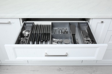 Open drawer with stainless steel utensil set. Order in kitchen Photo of Open drawer with stainless steel utensil set. Order in kitchen