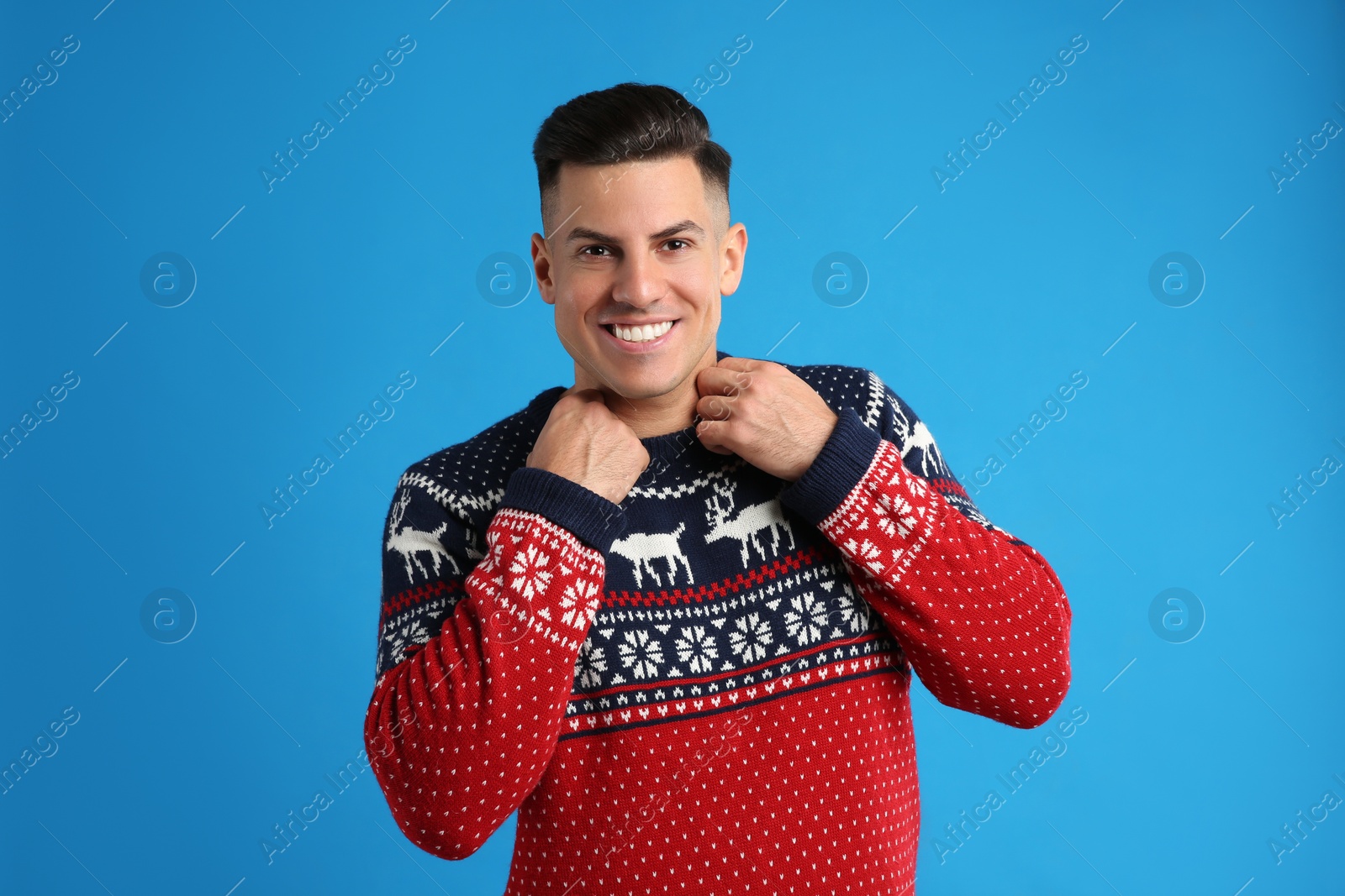 Handsome man in Christmas sweater on blue background Photo of Handsome man in Christmas sweater on blue background