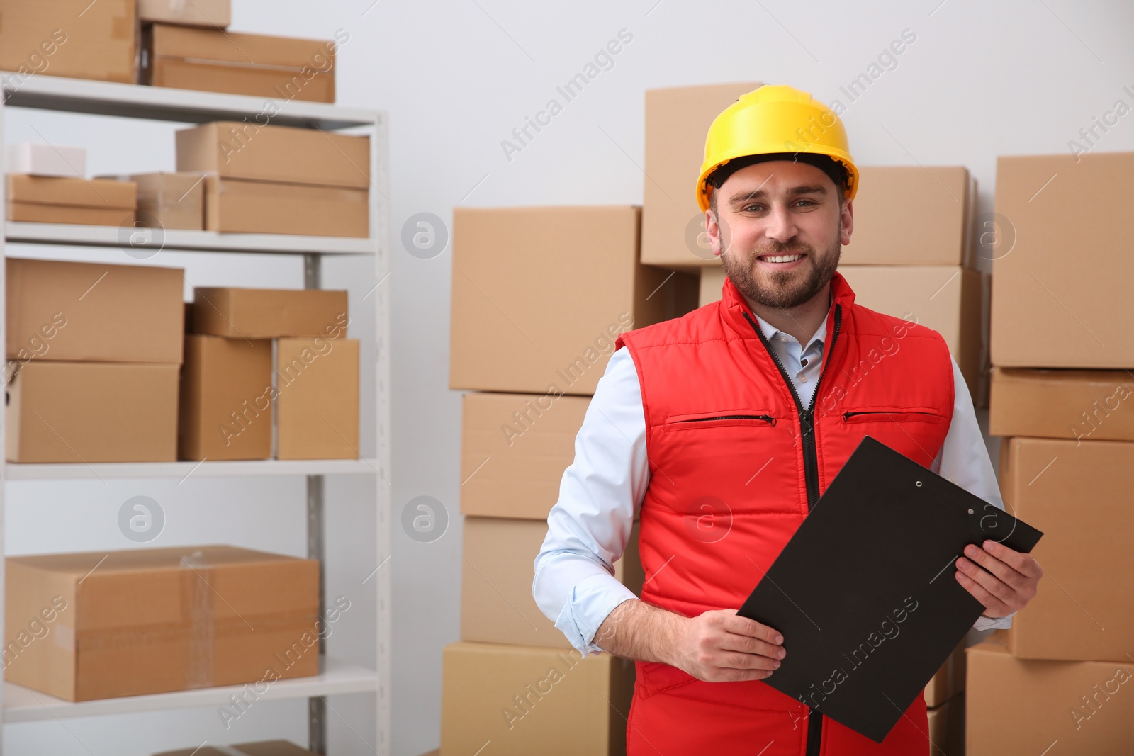 Photo of Young man with clipboard near cardboard boxes at warehouse