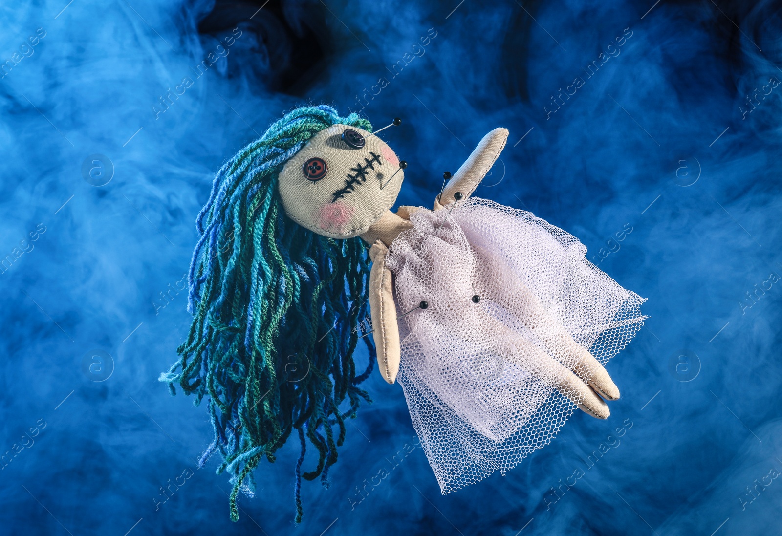 Female voodoo doll with pins and smoke on blue background Photo of Female voodoo doll with pins and smoke on blue background