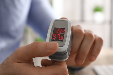 Man measuring oxygen level with modern fingertip pulse oximeter at workplace, closeup Photo of Man measuring oxygen level with modern fingertip pulse oximeter at workplace, closeup