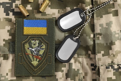 MYKOLAIV, UKRAINE - SEPTEMBER 26, 2020: Metal military ID tags, bullet shells and Ukrainian army patch on camouflage background, flat lay Photo of MYKOLAIV, UKRAINE - SEPTEMBER 26, 2020: Metal military ID tags, bullet shells and Ukrainian army patch on camouflage background, flat lay