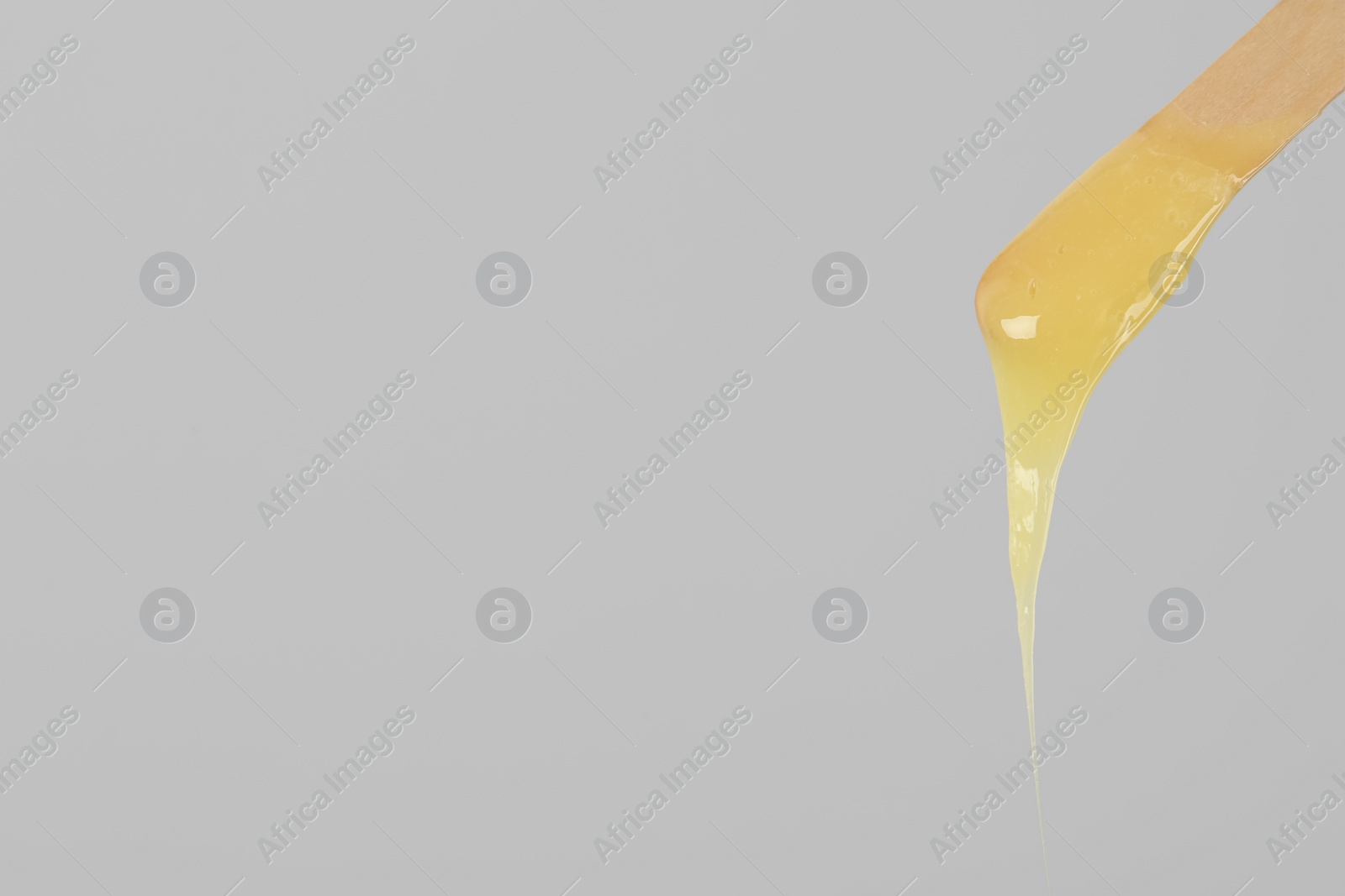 Wooden spatula with hot depilatory wax on light grey background. Space for text Photo of Wooden spatula with hot depilatory wax on light grey background. Space for text