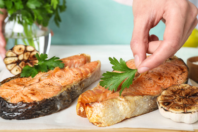 Woman adding parsley to cooked red fish on table, closeup Photo of Woman adding parsley to cooked red fish on table, closeup