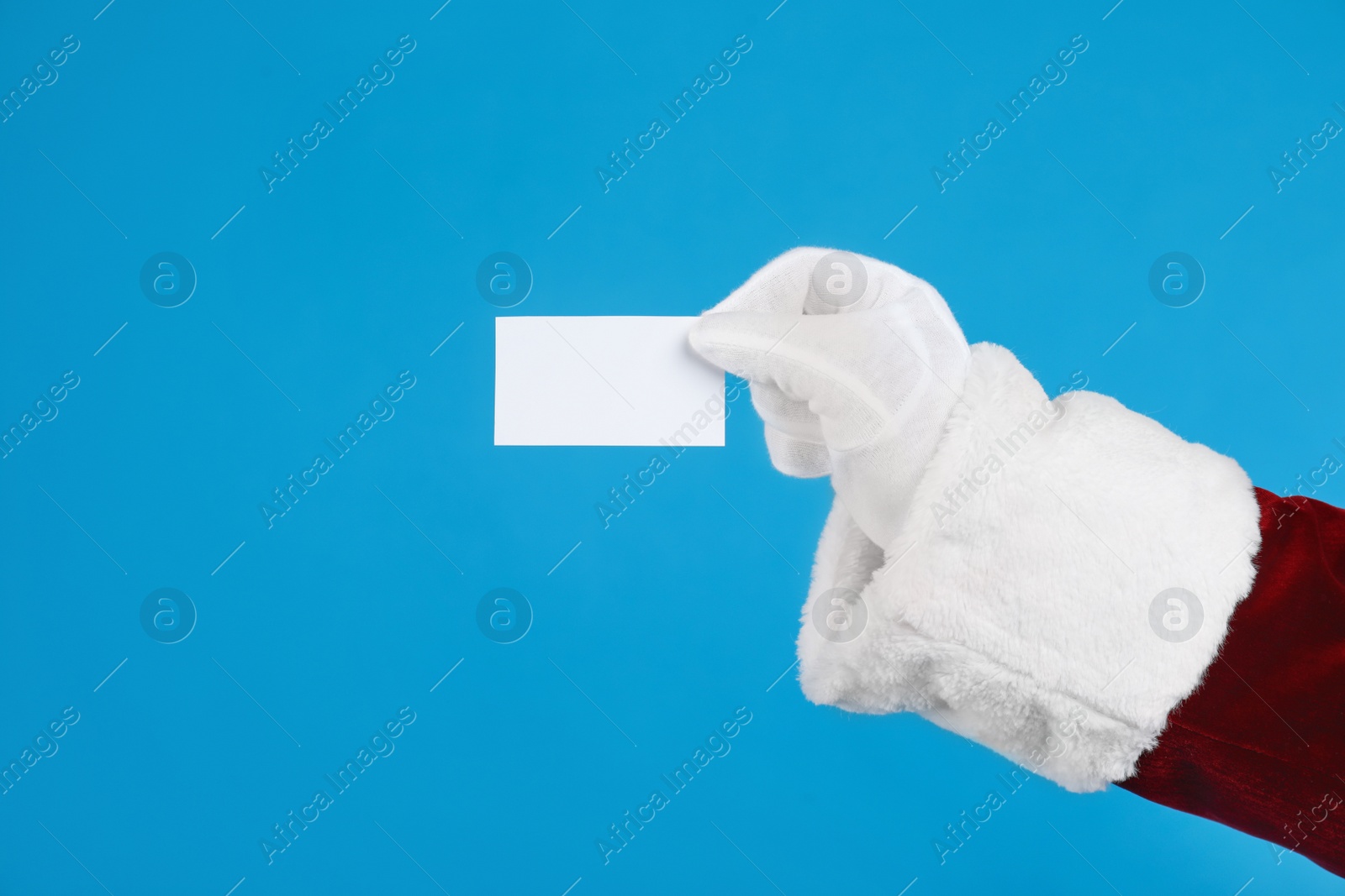 Santa Claus holding blank card on blue background, closeup of hand. Space for text Photo of Santa Claus holding blank card on blue background, closeup of hand. Space for text