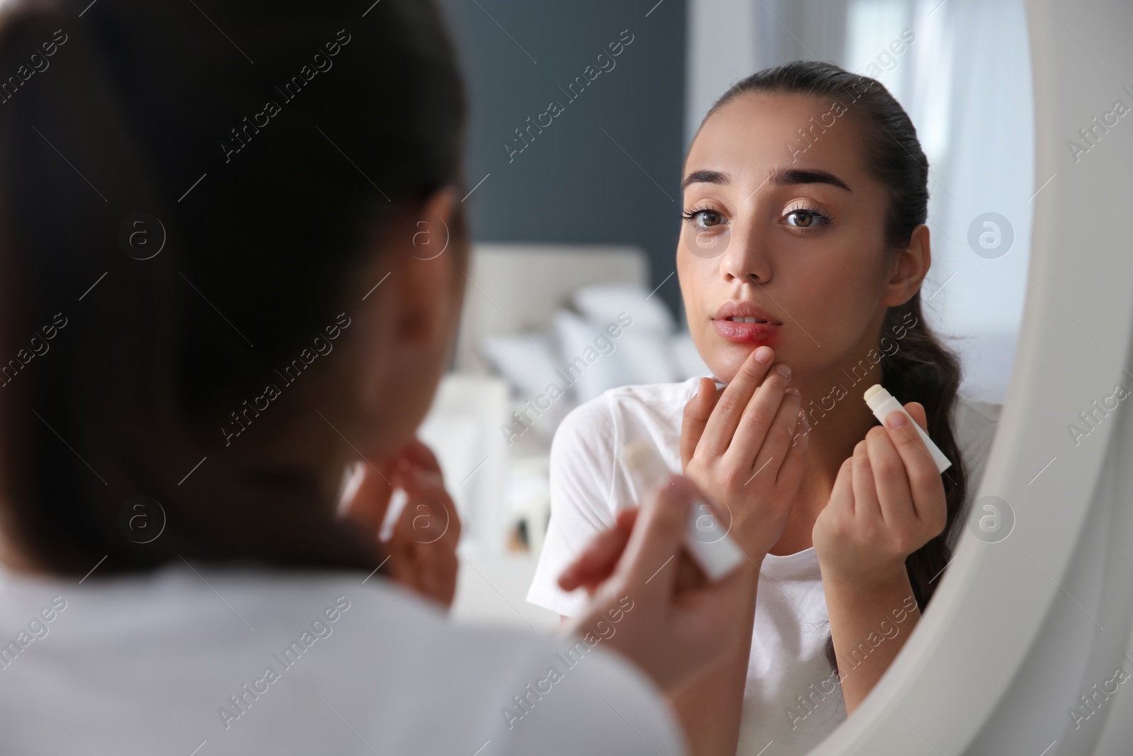 Young woman with herpes applying lip balm in front of mirror at home Photo of Young woman with herpes applying lip balm in front of mirror at home