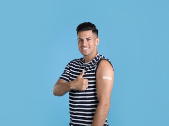 Vaccinated man with medical plaster on his arm showing thumb up against light blue background Photo of Vaccinated man with medical plaster on his arm showing thumb up against light blue background