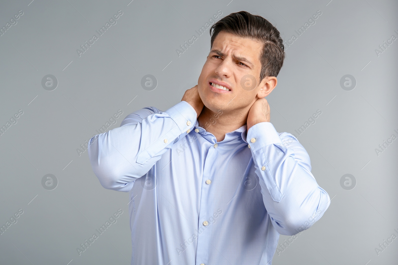 Young man suffering from neck pain on grey background Photo of Young man suffering from neck pain on grey background