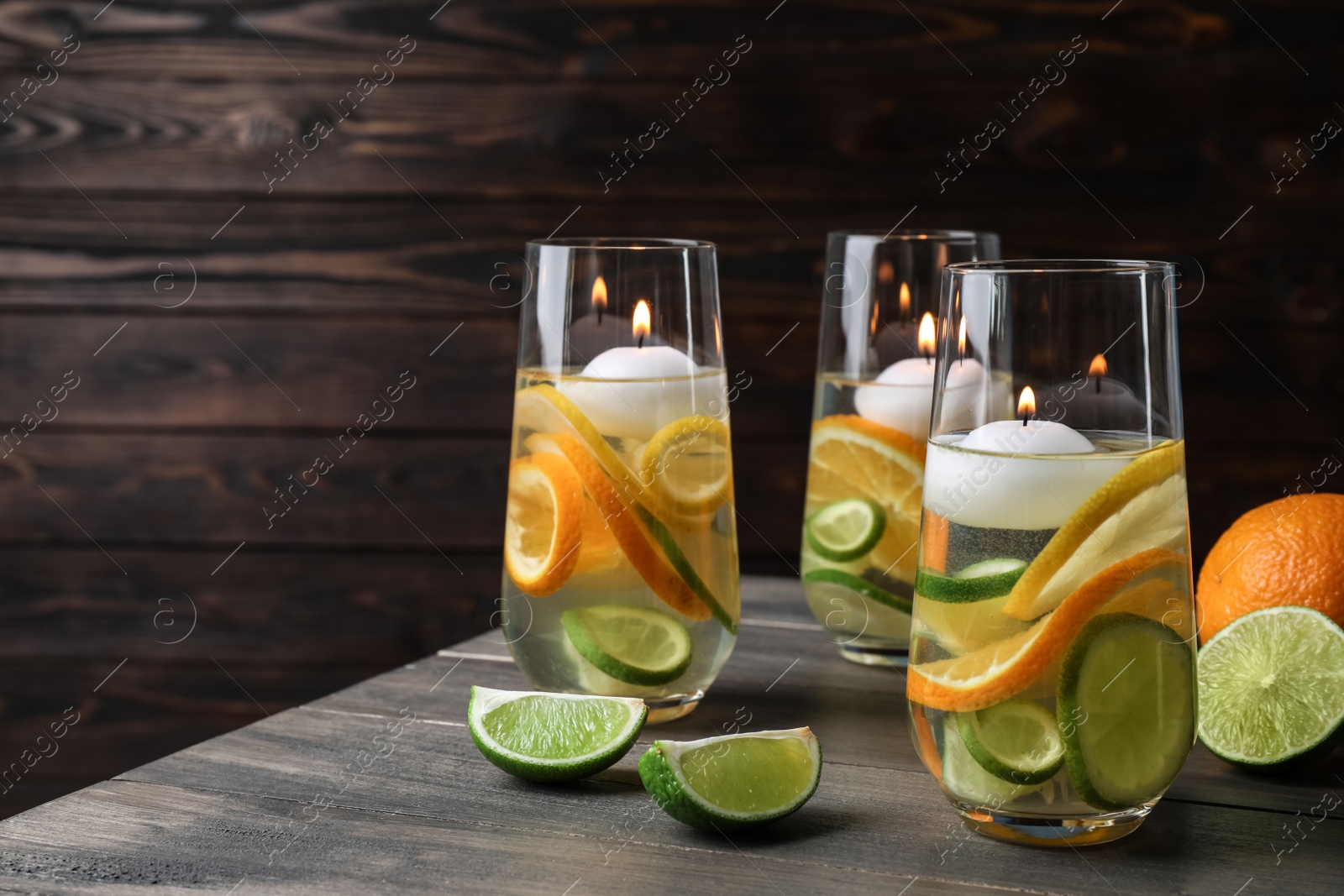 Candles and fruit slices in glass holders with liquid on wooden table Photo of Candles and fruit slices in glass holders with liquid on wooden table