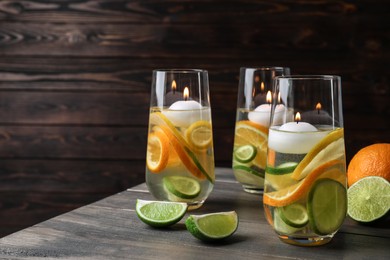 Candles and fruit slices in glass holders with liquid on wooden table Photo of Candles and fruit slices in glass holders with liquid on wooden table