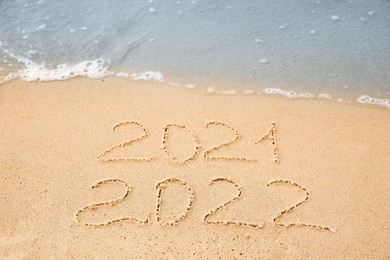 Dates written on sandy beach. 2021 washed by sea wave as New 2022 Year coming Photo of Dates written on sandy beach. 2021 washed by sea wave as New 2022 Year coming