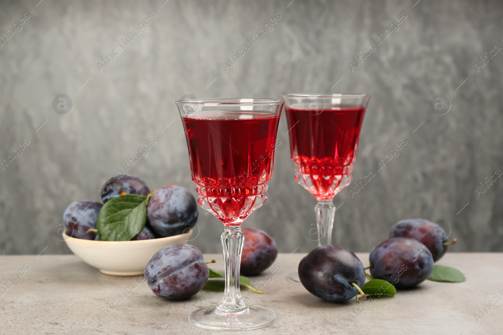 Delicious plum liquor and ripe fruits on table against grey background. Homemade strong alcoholic beverage Photo of Delicious plum liquor and ripe fruits on table against grey background. Homemade strong alcoholic beverage