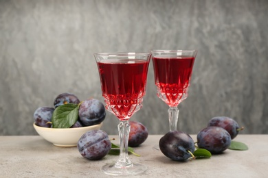 Delicious plum liquor and ripe fruits on table against grey background. Homemade strong alcoholic beverage Photo of Delicious plum liquor and ripe fruits on table against grey background. Homemade strong alcoholic beverage