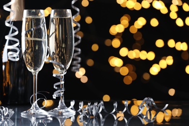 Glasses and bottle of champagne with serpentine streamers against blurred lights on black background. Space for text Photo of Glasses and bottle of champagne with serpentine streamers against blurred lights on black background. Space for text