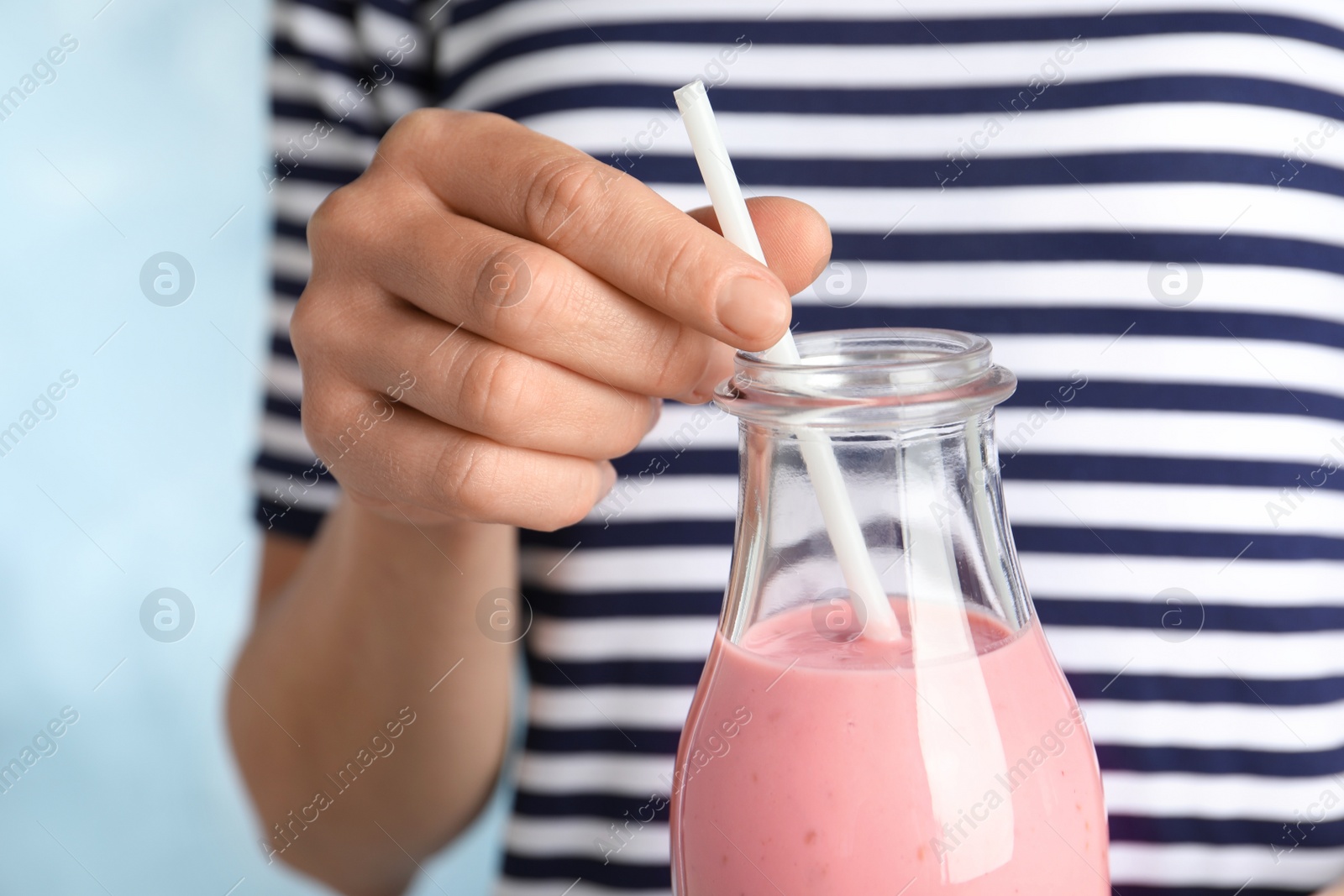 Woman with glass bottle of tasty smoothie on light blue background, closeup Image of Woman with glass bottle of tasty smoothie on light blue background, closeup