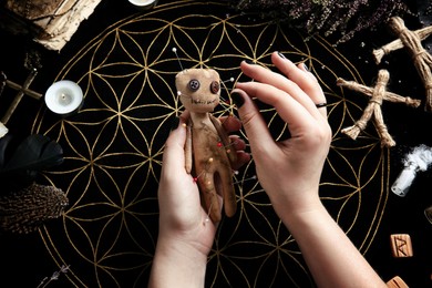 Photo of Woman stabbing voodoo doll with needle at table, closeup. Curse ceremony