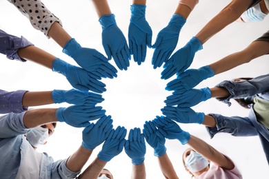 People in blue medical gloves joining hands on light background, low angle view Photo of People in blue medical gloves joining hands on light background, low angle view