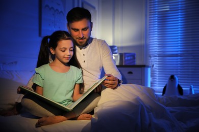 Father with little daughter reading fairy tale in dark bedroom Photo of Father with little daughter reading fairy tale in dark bedroom