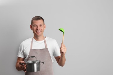 Happy man with cooking pot and ladle on light grey background. Space for text Photo of Happy man with cooking pot and ladle on light grey background. Space for text