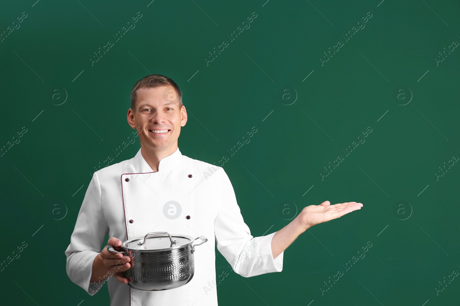 Happy male chef with cooking pot on dark green background. Space for text Photo of Happy male chef with cooking pot on dark green background. Space for text
